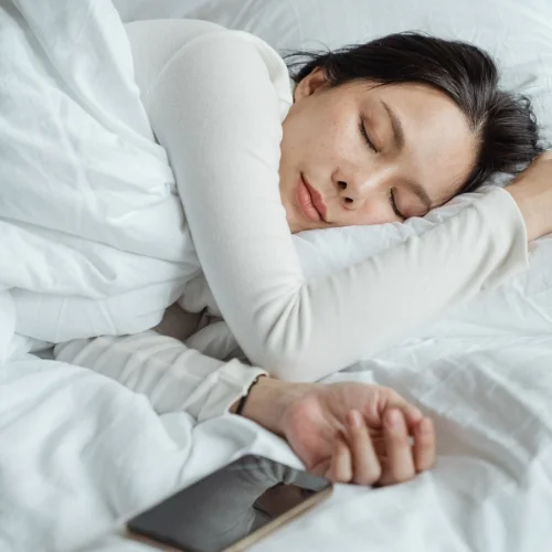 Woman sleeping peacefully in bed with a smartphone resting beside her.