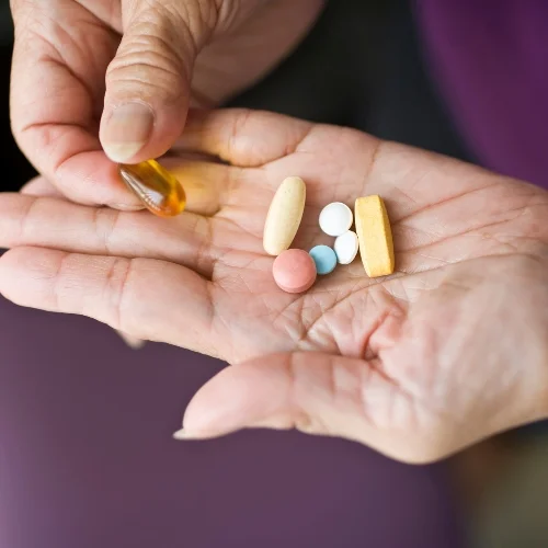 Hands holding a variety of pills and supplements.